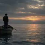 Persona di spalle in piedi su una barca a remi di legno, in un mare grigio e calmo al tramonto