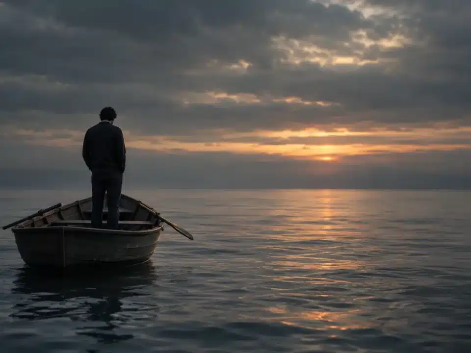 Persona di spalle in piedi su una barca a remi di legno, in un mare grigio e calmo al tramonto